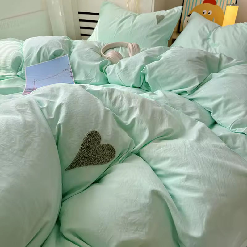 Twin bed with mint green cotton duvet and flat sheet in sunlight.
