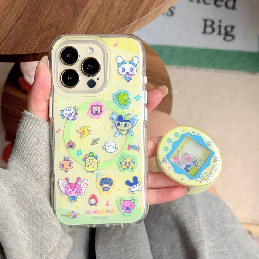Phone case with cartoon characters held by a person, with a green checkered bag in the background.