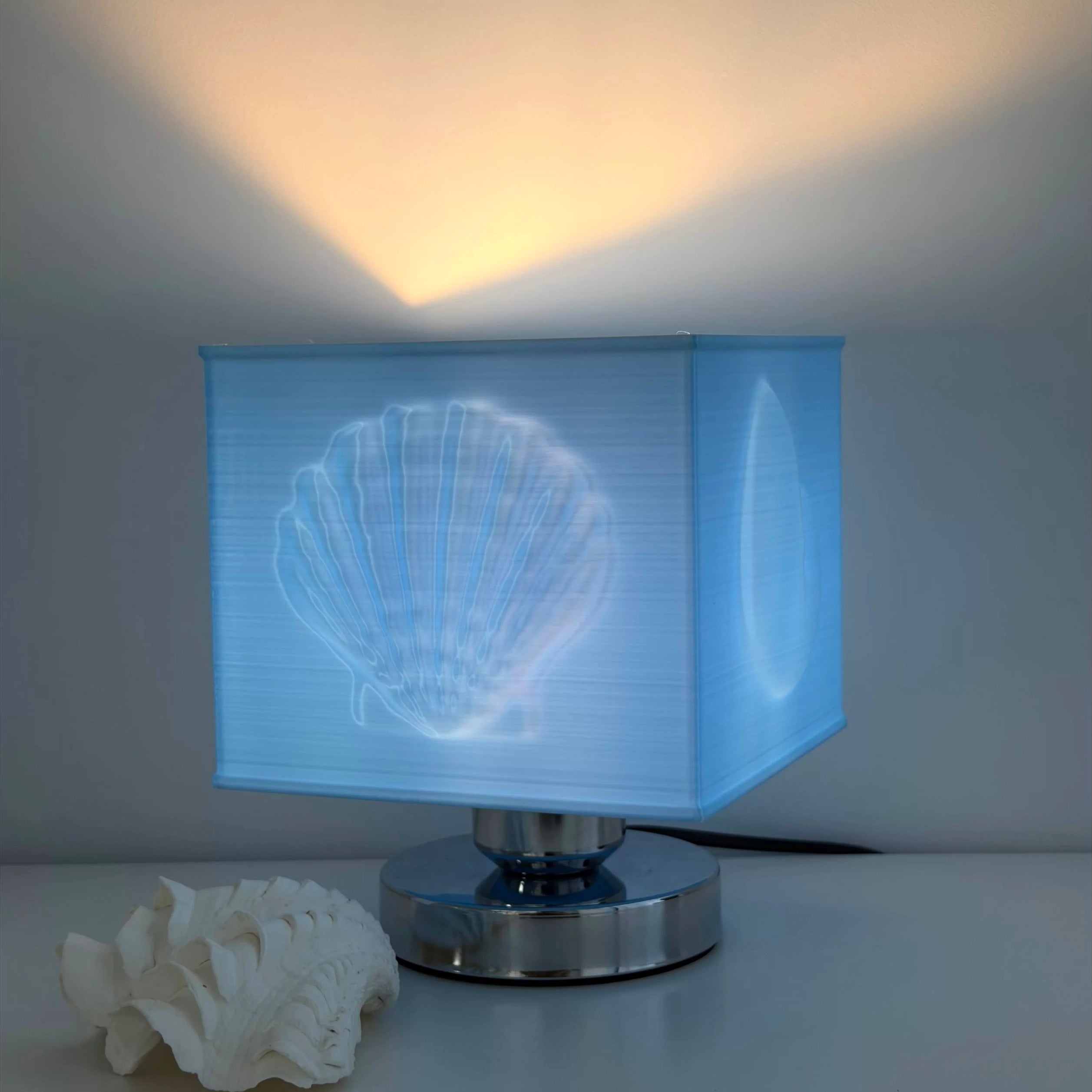 Table lamp with shell design on the shade, next to a white shell on a light background