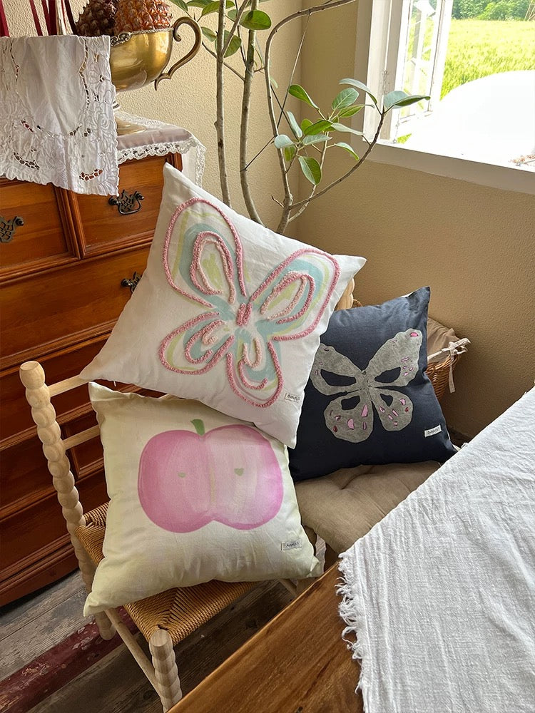 Accent pillows with pastel butterfly, gray butterfly and apple prints in a sunny corner