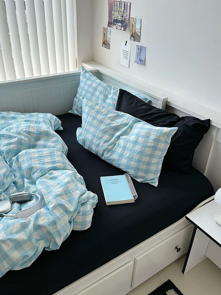 Bed with blue checkered bedding and pillows in a room with white walls and a window.