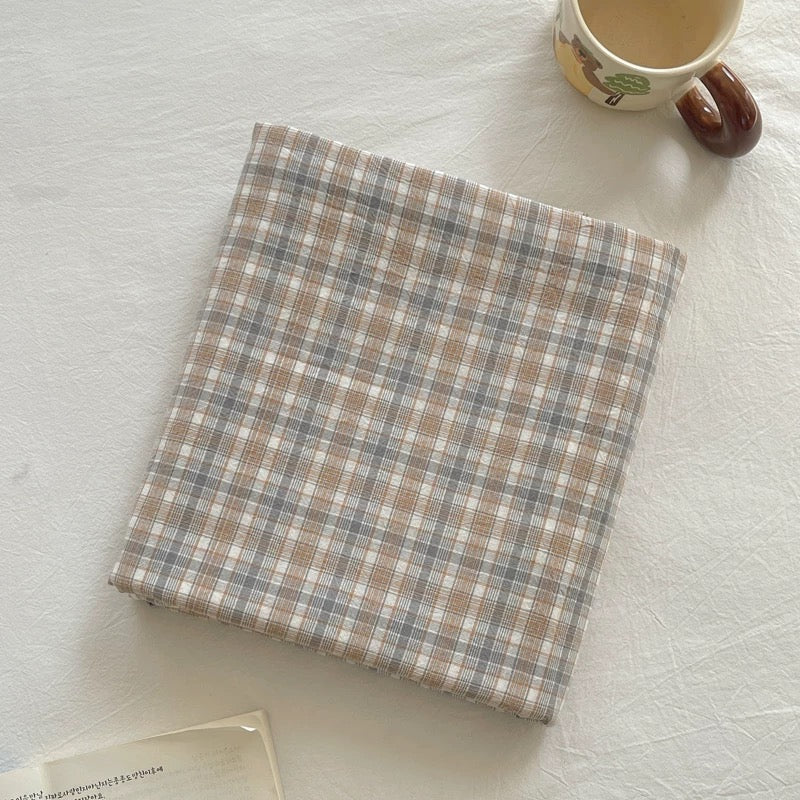 Plaid fabric on a textured surface with a mug in the corner