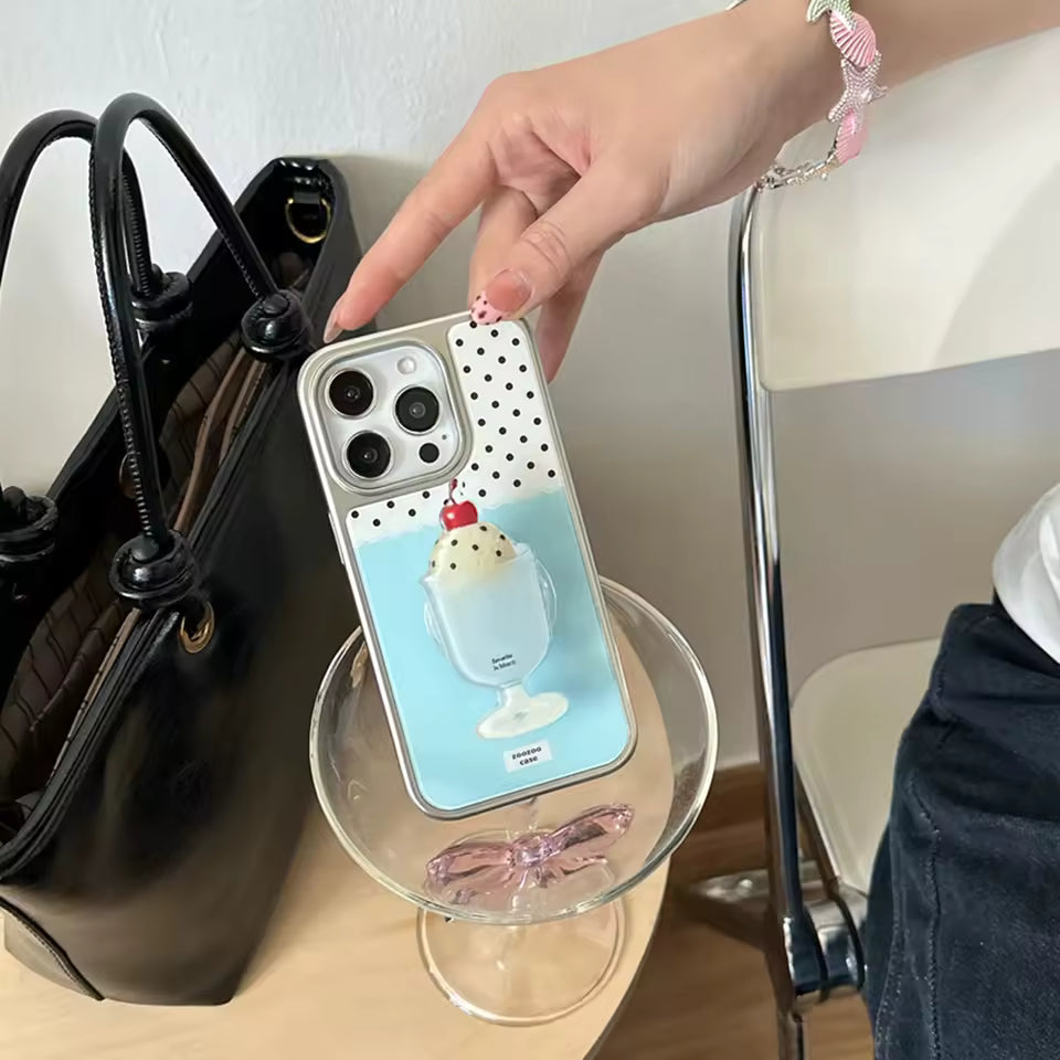 Phone case with ice cream design held by a hand next to a black handbag.