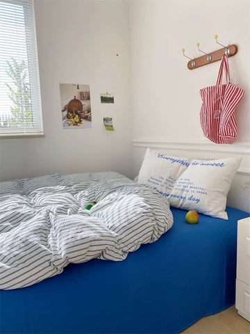 Bedroom with blue bedspread, striped comforter, and decorative pillows.