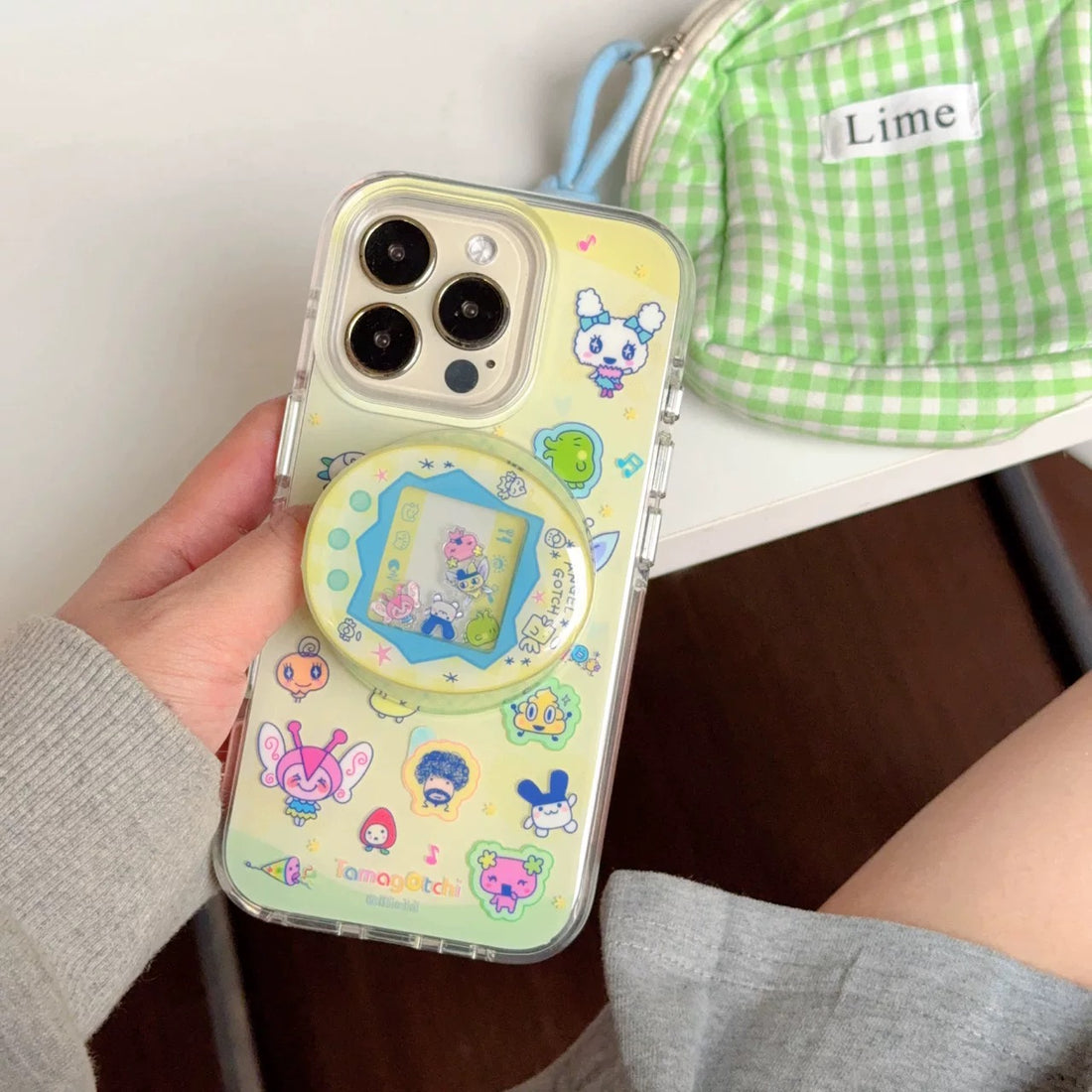 Phone case with cartoon characters held by a person, with a green checkered bag in the background.