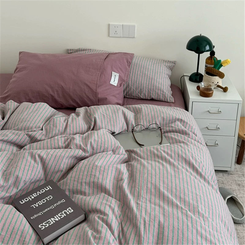 Bed with striped bedding and a nightstand with a lamp and small figurine.