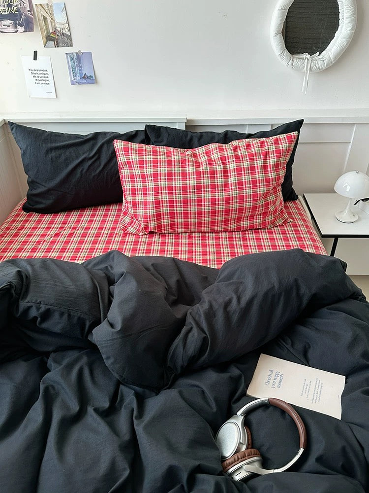 Bed with black comforter, red plaid pillow, and a watch on a nightstand.