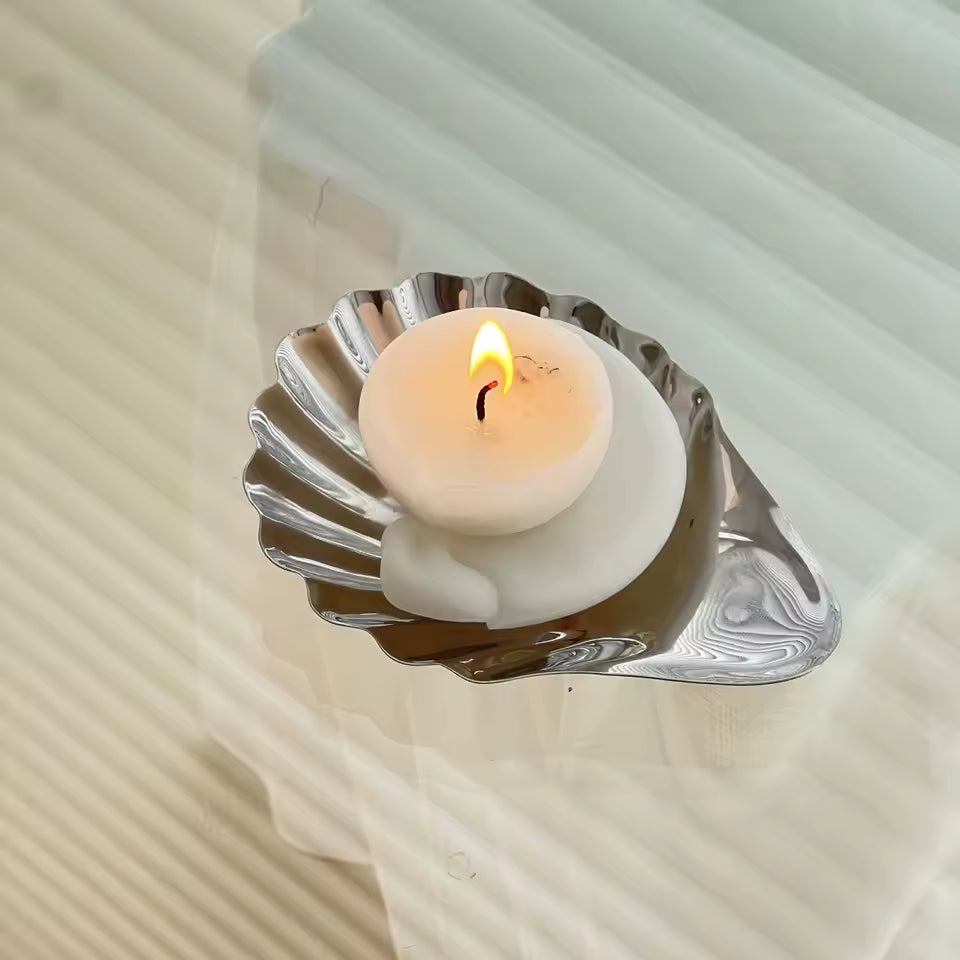 Candle in a shell-shaped metal holder on a textured surface