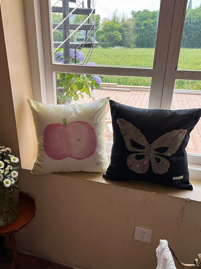 Painted apple and gray butterfly embroidered throw pillows styled on a sunny window seat