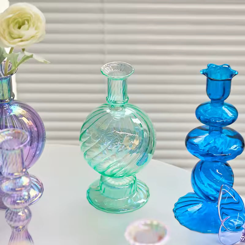 Set of colorful glass vases with a white flower against a neutral background