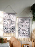 The Sun and Moon hanging side by side on a minimalist white wall with plant accents.
