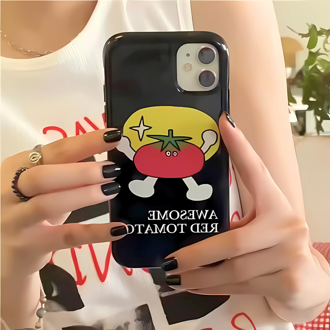 Person holding a phone with a cartoon tomato design on a black case.