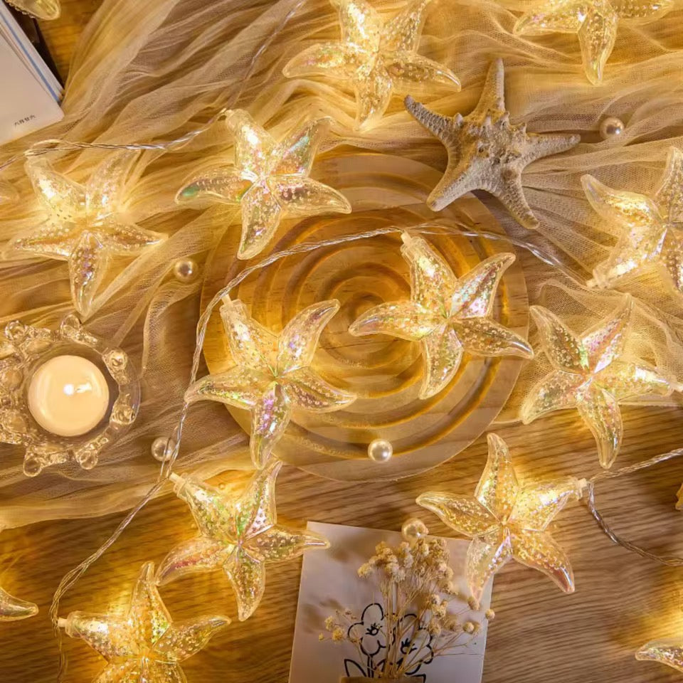 Star-shaped string lights on a decorative surface with a candle and feathers.