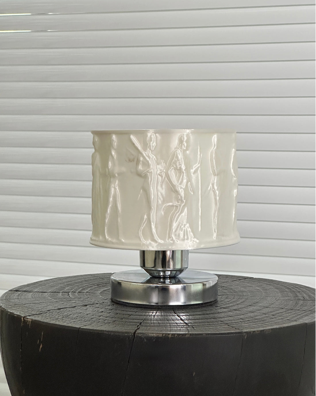 Table lamp with a textured white shade on a wooden base against a window blind background