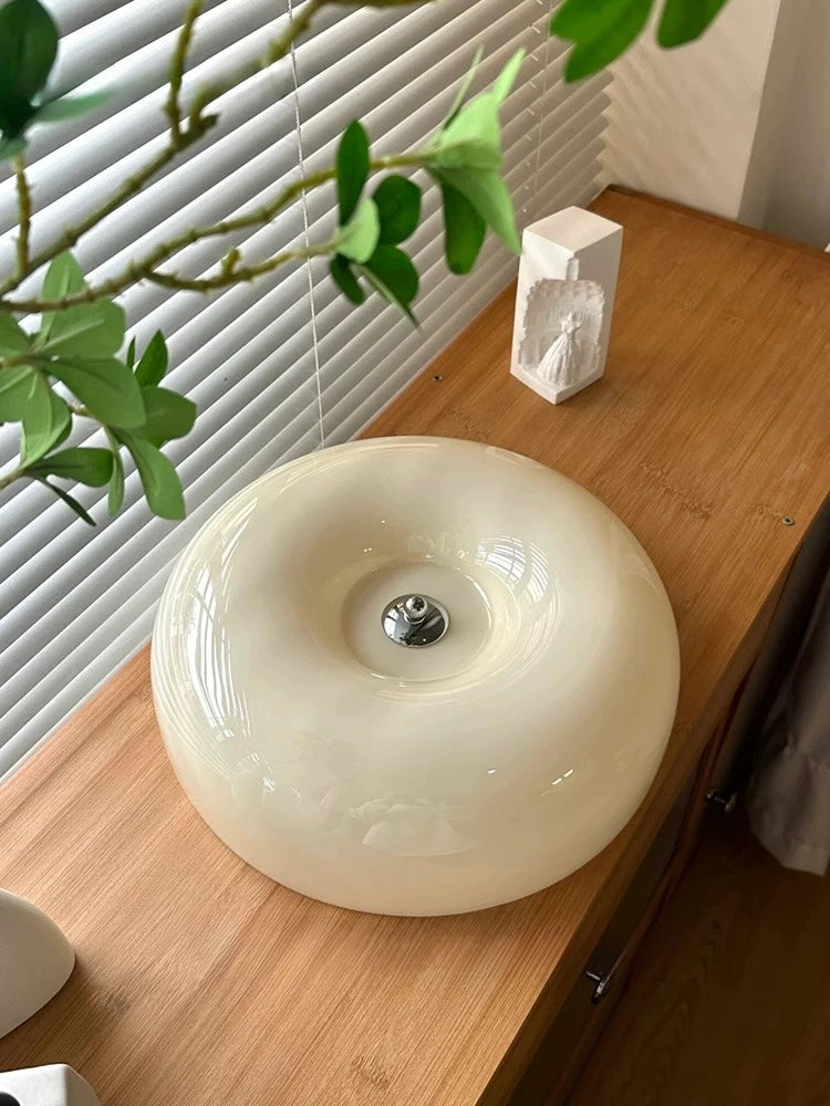 White ceramic object on a wooden surface with a plant in the background