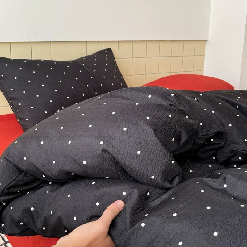 Preppy black polka dot bedding styled with red accents in minimalist dorm bedroom