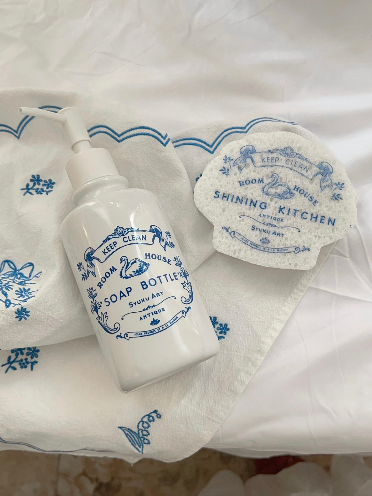 Blue and white soap dispenser lies beside a scalloped sponge, showing the swan artwork on the front.