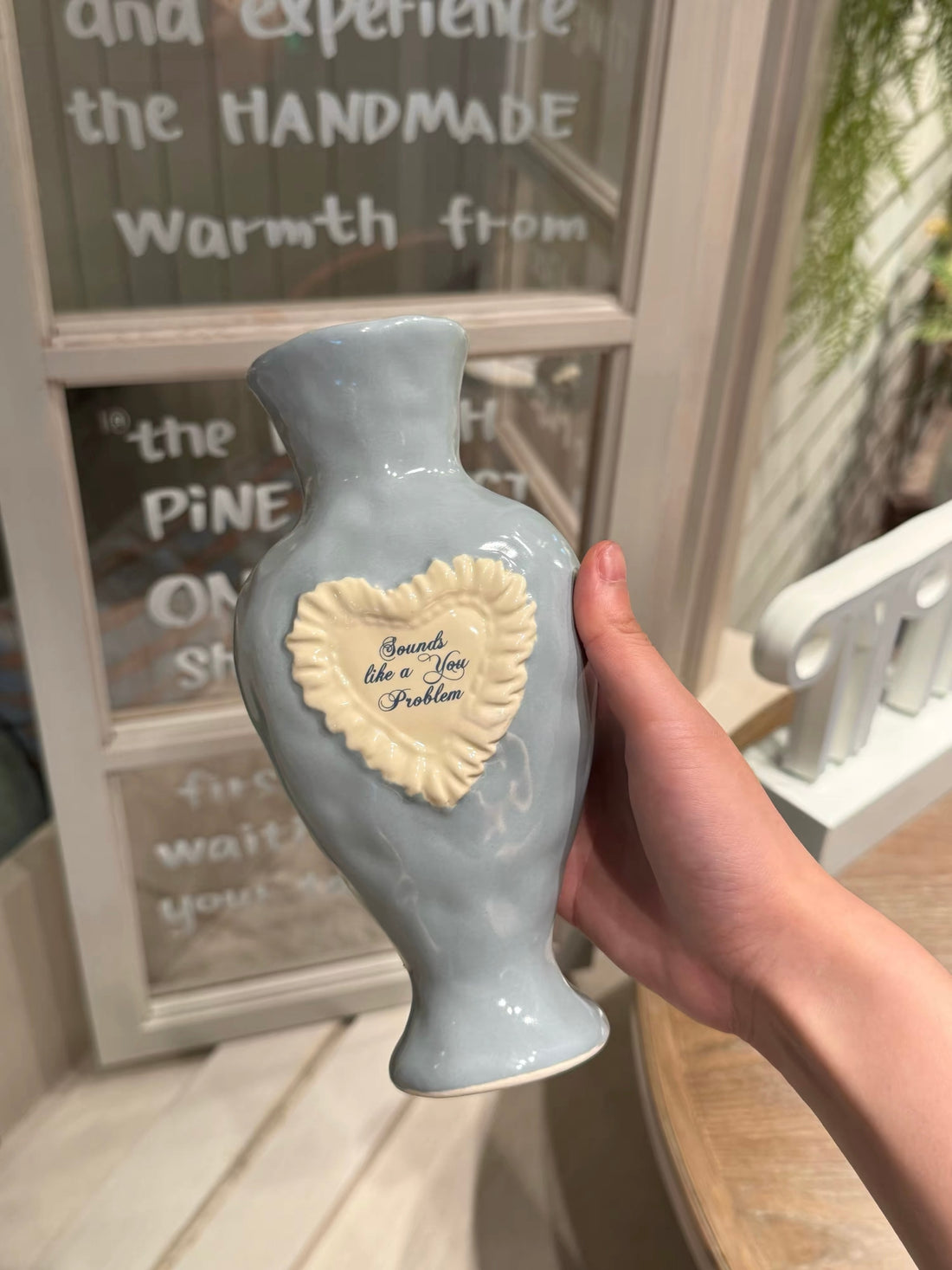 Blue vase standing on a pale green box, with a raised white heart, blue script and a flared foot below the body.