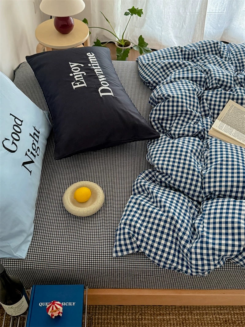 Bed with checkered duvet, pillows, and a small table with decor items.