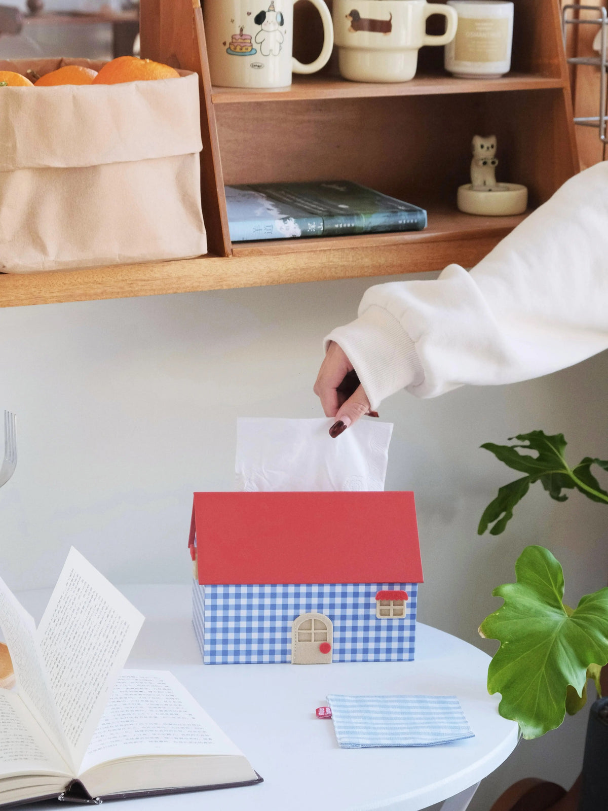 Blue checkered house shaped tissue box cover with red roof on a desk