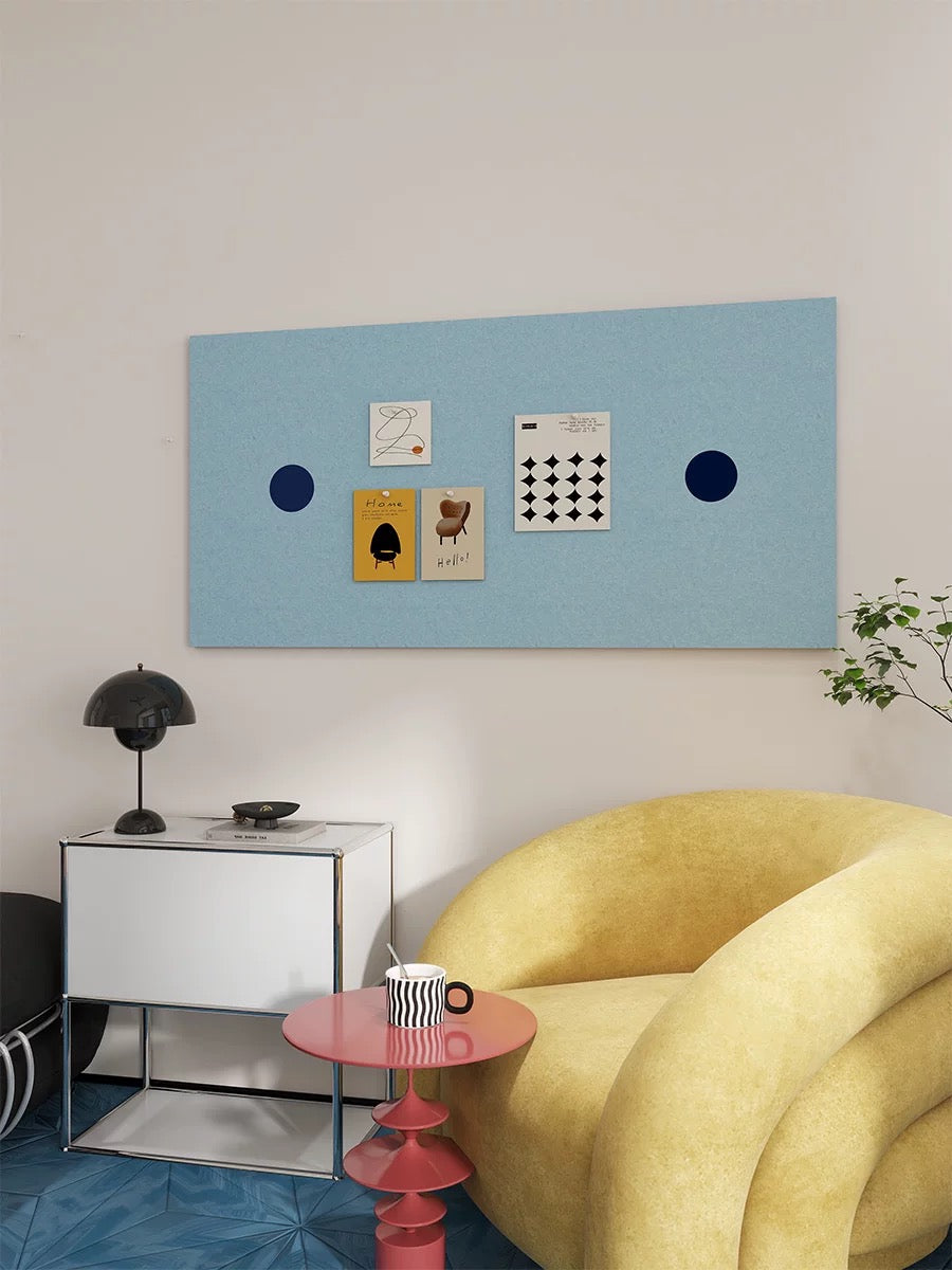 Light blue dotted bulletin board displaying prints above a white cabinet beside a yellow armchair.