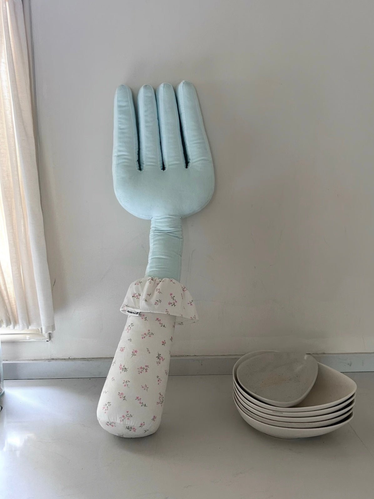 A blue fork pillow stands upright, with a light floral handle and a gathered collar beneath its long tines.