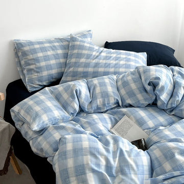 Light blue and white plaid bedding set with matching pillowcases and a duvet cover, styled on a bed with dark pillows and a book resting on the duvet.