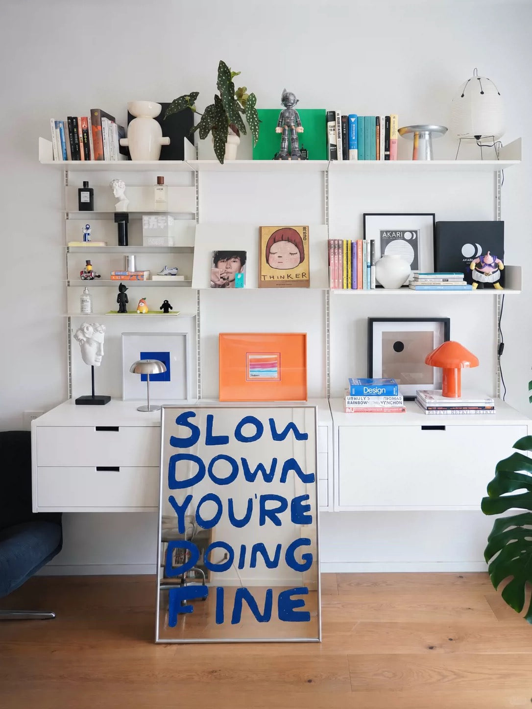 A blue lettering mirror stands below open shelves, with large handwritten words filling the rectangular surface.