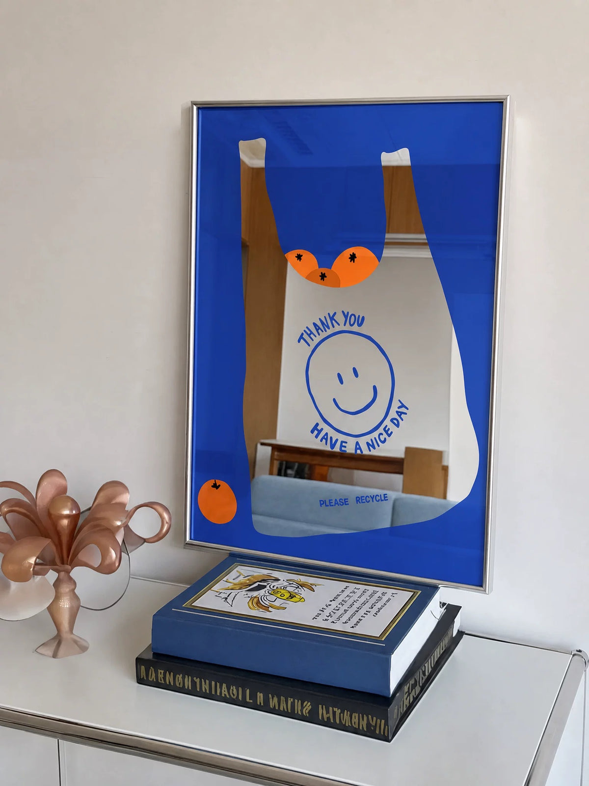 A blue orange bag mirror rests at an angle, showing a white grocery bag, orange fruit and blue printed lettering.