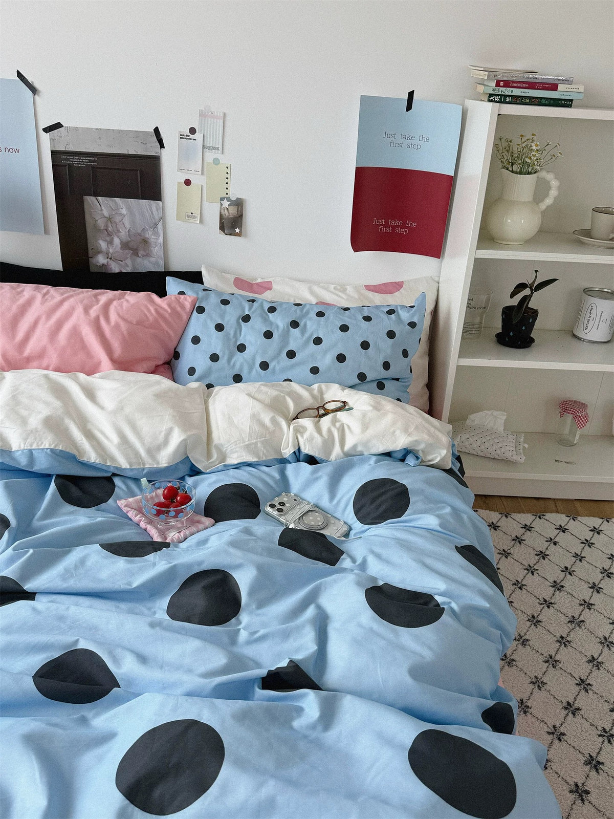 A front view of the bed shows black, plain pink and small dotted blue pillows above the large dotted cover.