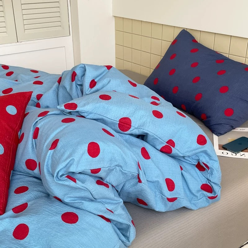 Preppy blue polka dot duvet cover with red dots shown in a minimalist bedroom aesthetic with clean styling.