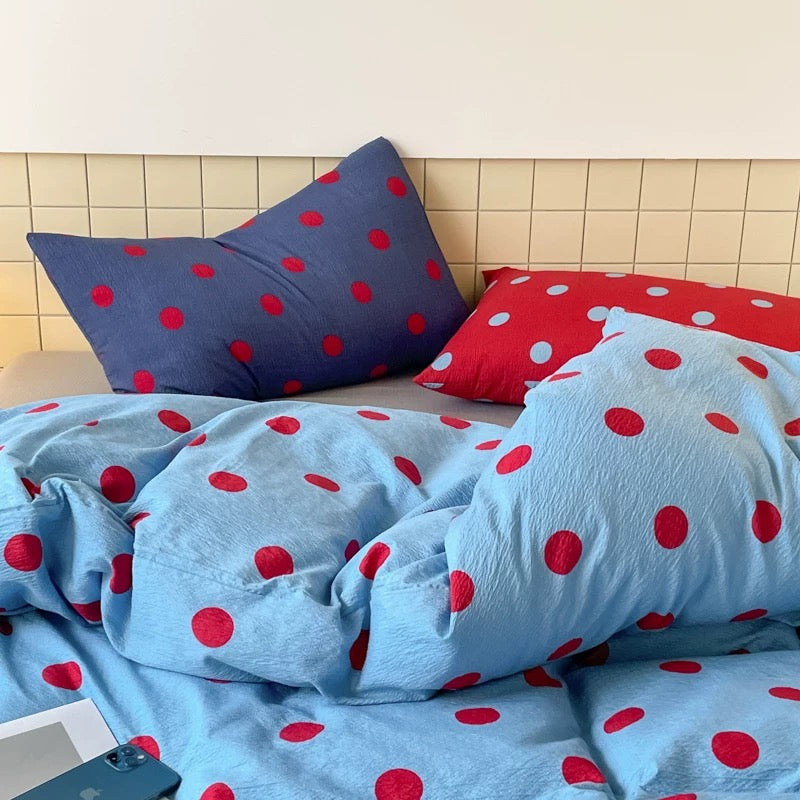 Blue polka dot bedding set with red dots styled in a cozy preppy bedroom with soft pillows and duvet cover.