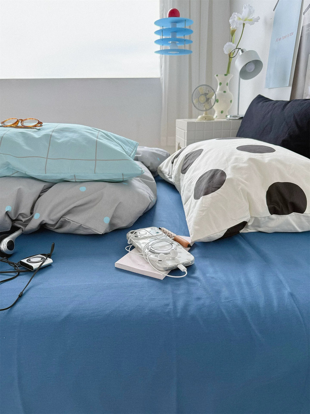 Blue check and black dot pillowcases beside a black pillow on a blue bed.
