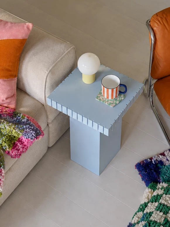 Light blue small side table with a striped mug and a white lamp beside a beige sofa and an orange leather chair