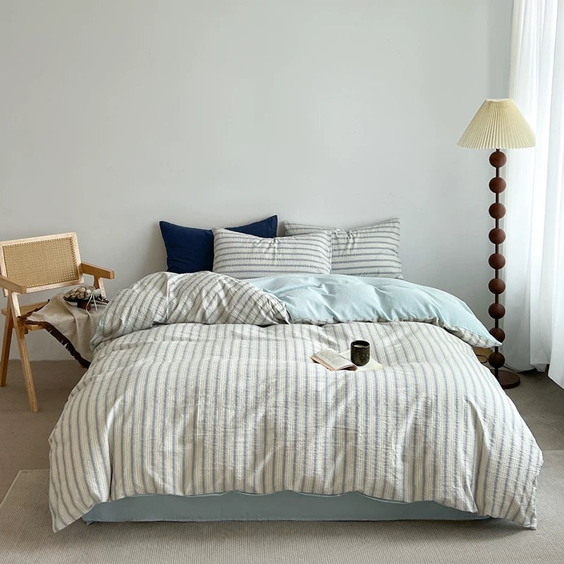 Rumpled seafoam blue duvet cover and striped pillowcases piled together on a cozy unmade bed