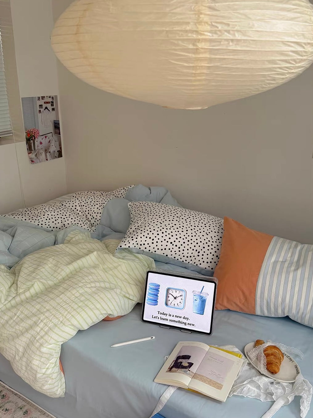 Blue and yellow bedding is seen beneath a paper lamp, with books and a tablet on the blue sheet.
