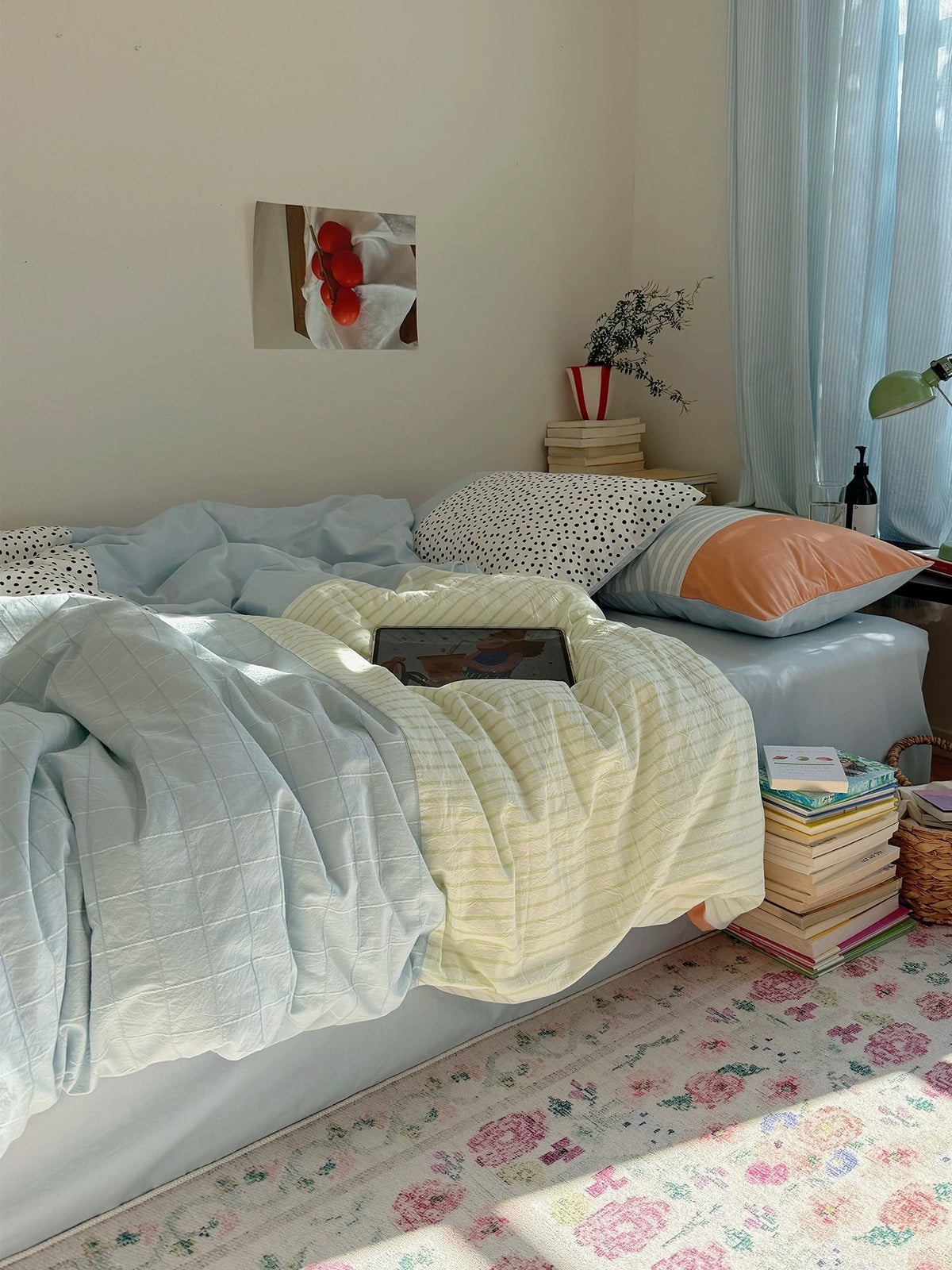 A blue and yellow bedding set is spread across a bed beside a window, with dotted and peach-panel pillows.