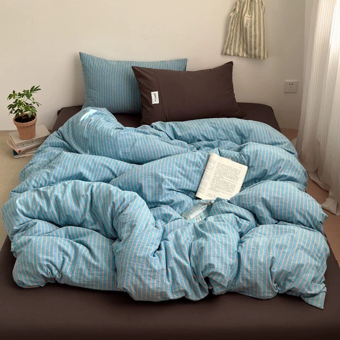 Blue striped comforter on a bed with pillows and a book in a bedroom setting.