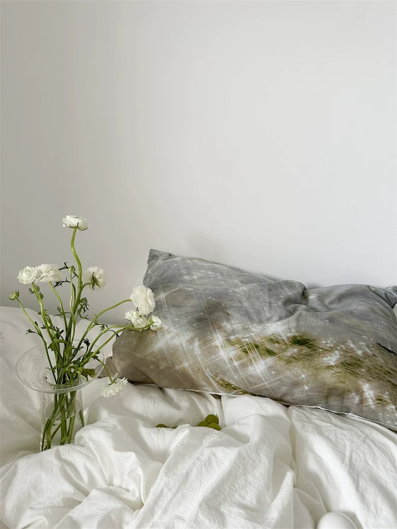 Person holding a white pillowcase with a black cat design on a bed.