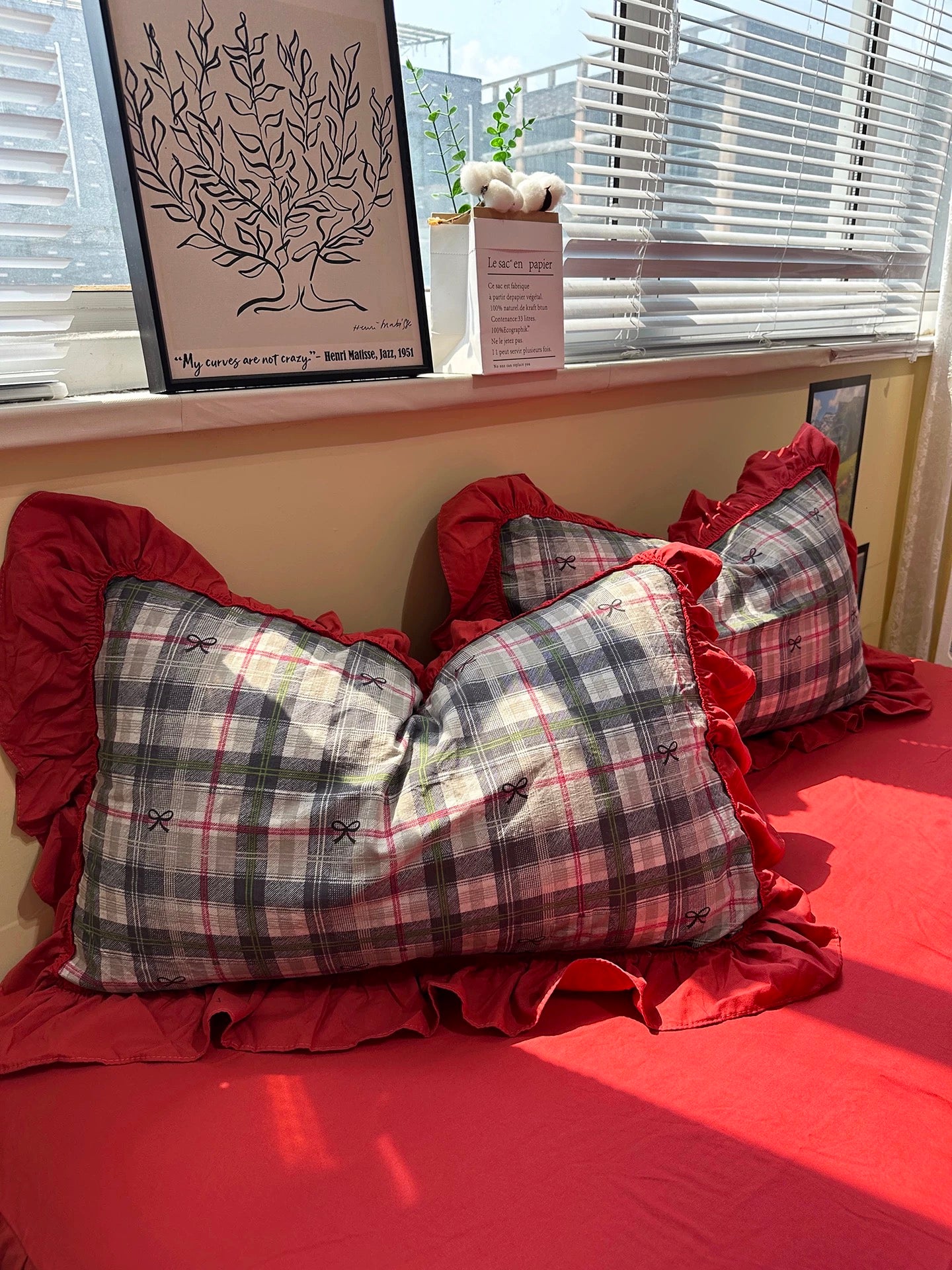 Plaid pillows on a red bedspread with a window in the background