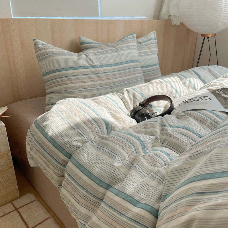 Blue striped cotton bedding set styled on minimal wood bed with neutral Nordic bedroom decor lighting