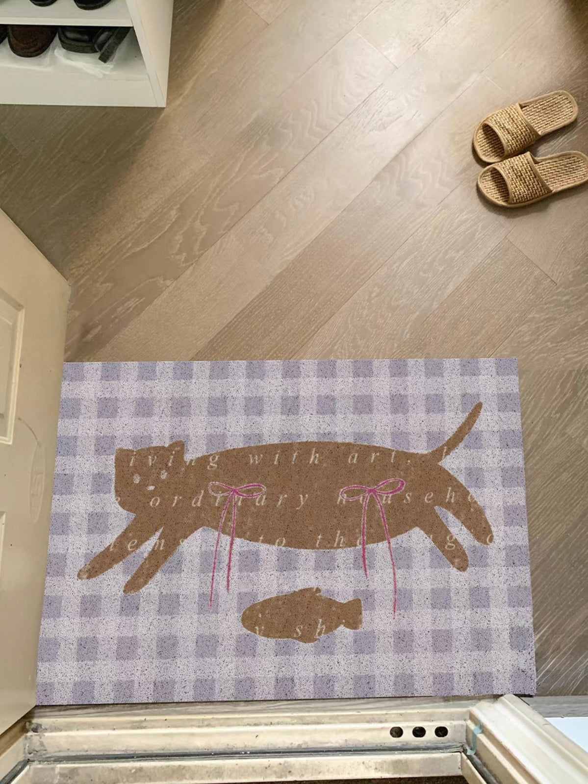 A cat doormat sits across the threshold with purple checks, a brown cat, a small fish and pink bows.