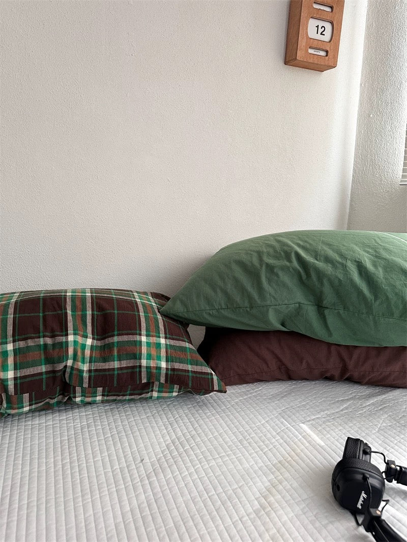 A green pillowcase rests over a cocoa brown design beside a plaid pillowcase.