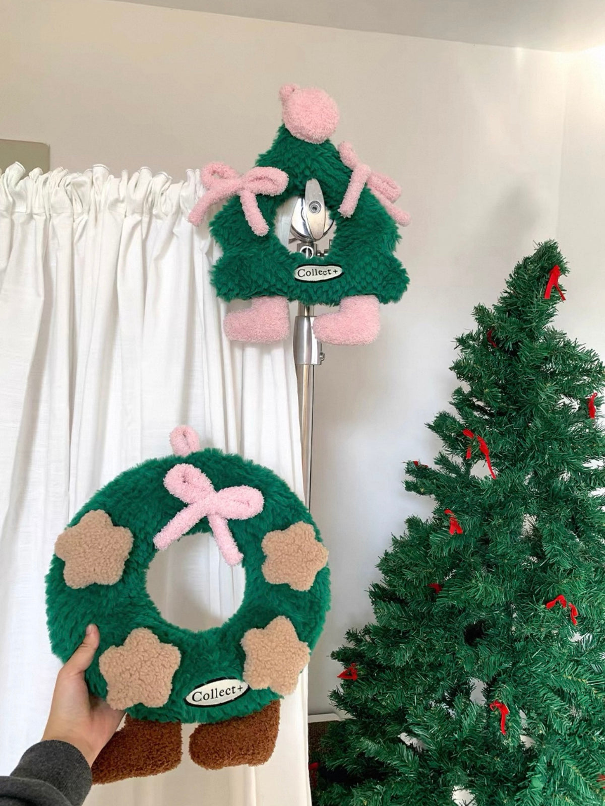 Green Christmas wreath pillow displayed near a decorated Christmas tree and white curtains