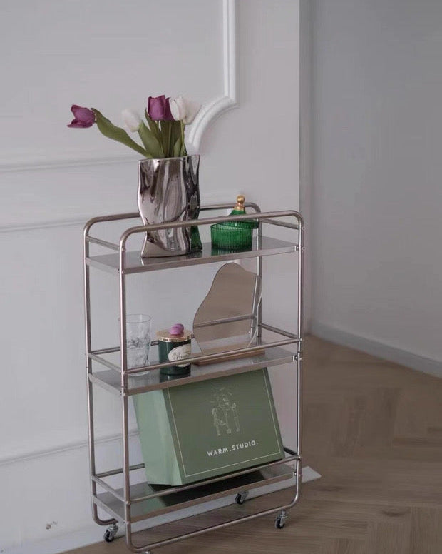 Modern chrome storage cart for small space organization with books, cups, and decorative objects.