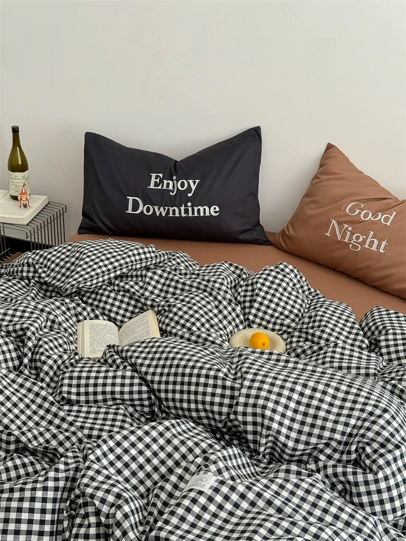 Bed with checkered duvet, pillows with text, and a bottle on a nightstand.