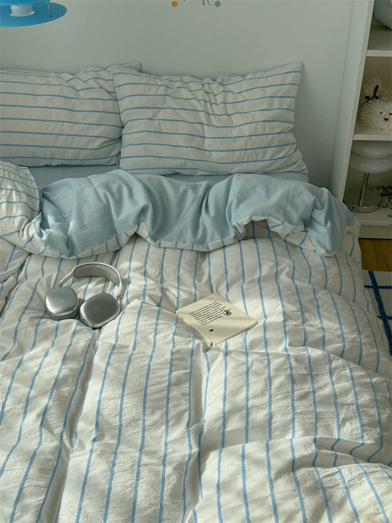 Striped bedding on a bed with a white wall and shelf in the background