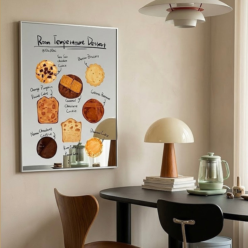 A framed wall art print titled 'Room Temperature Dessert' hangs on a beige wall above a dining table with chairs, a mushroom-shaped table lamp, books, and a glass teapot. The print features illustrated desserts with handwritten labels.
