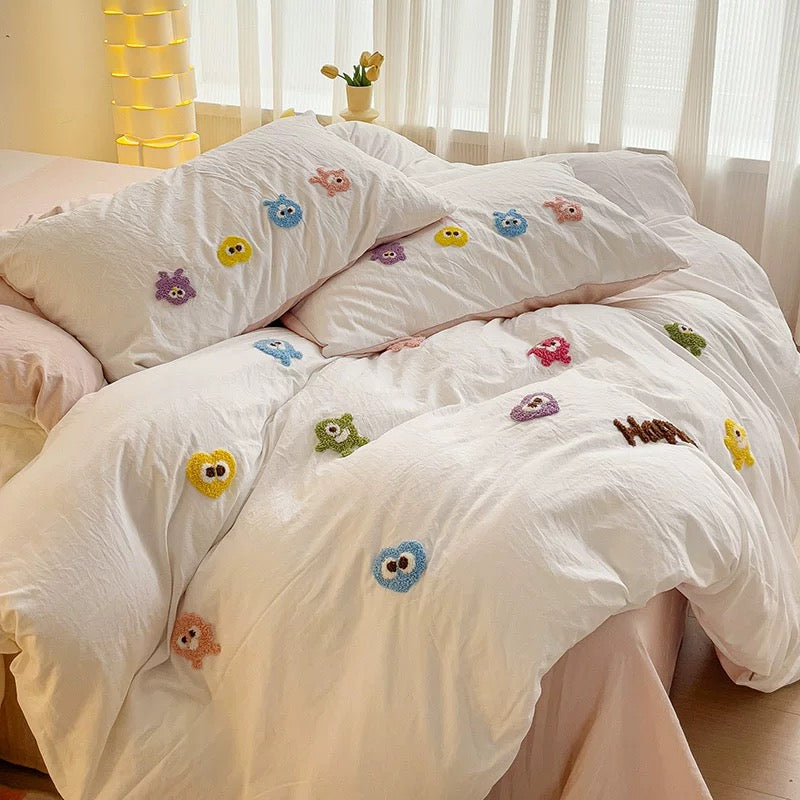 Close bed view of white duvet and pillowcases covered with small colorful embroidered cartoon characters.
