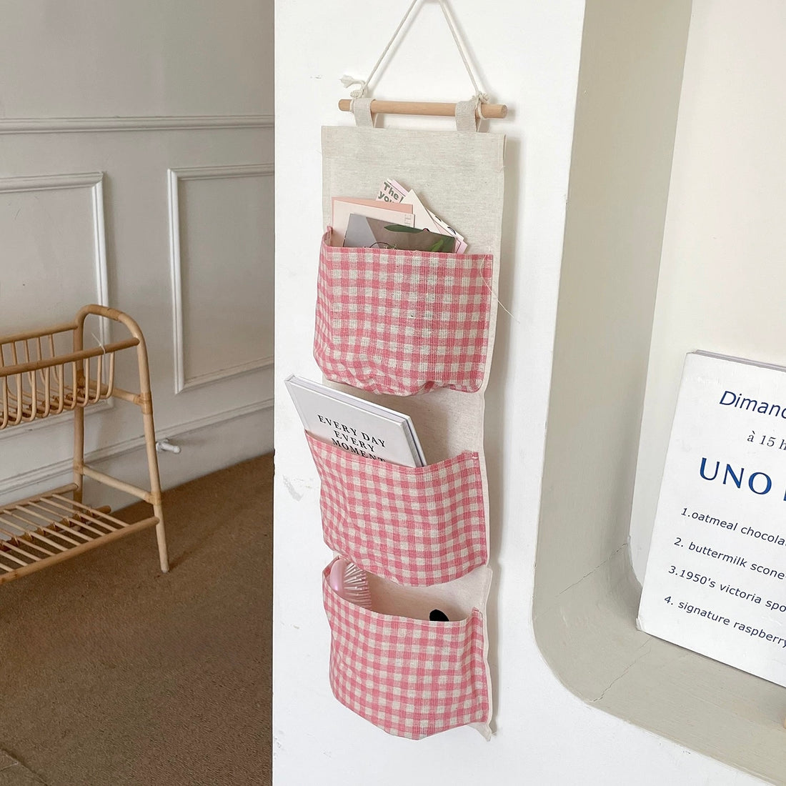 Hanging organizer with pink gingham design on a white wall next to a table with a cake.